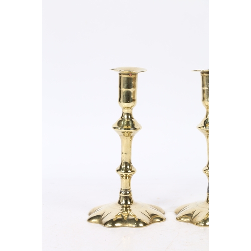 239 - A PAIR OF GEORGE II BRASS CANDLESTICKS. with a broad flange above a knopped stem set on a star petal... 