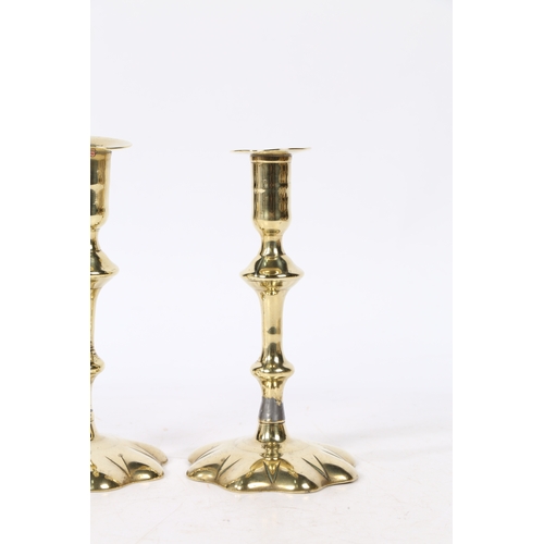 239 - A PAIR OF GEORGE II BRASS CANDLESTICKS. with a broad flange above a knopped stem set on a star petal... 