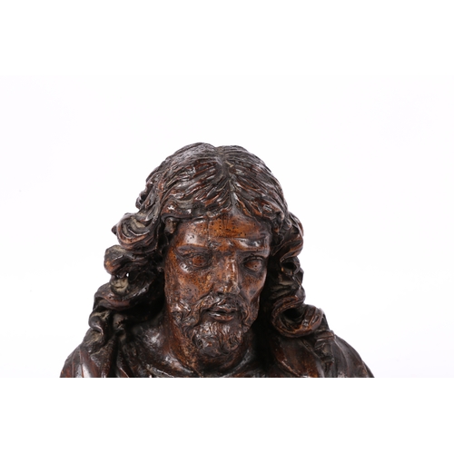 96 - A 17TH CENTURY WALNUT C ARVED BUST OF CHRIST. Flowing curled hair above wearing robes, 37cm high.