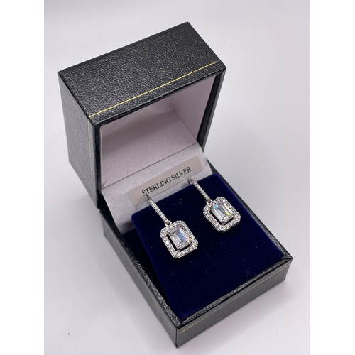 296 - A pair of silver and cubic zirconia drop earrings, set with rectangular-cut stone within a border of... 