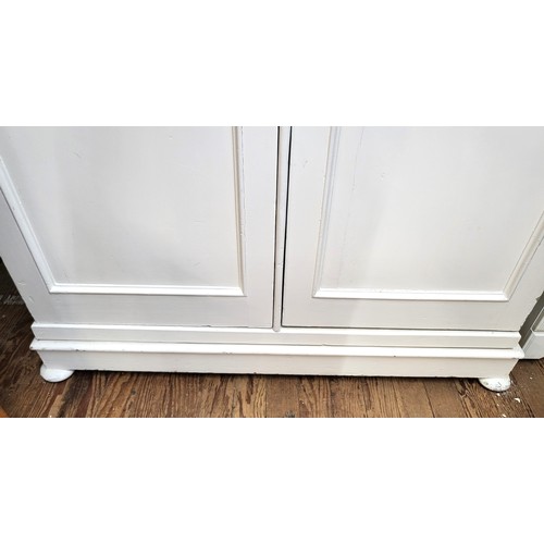 3 - A large two-door wardrobe, painted white and with a hanging rail. The wardrobe sits on a plinth on b... 