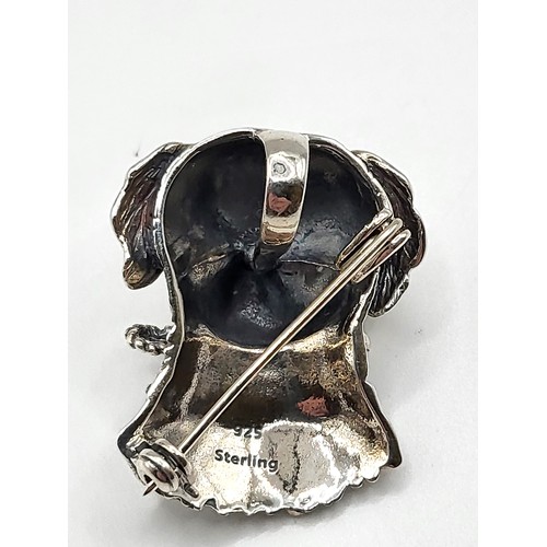 256 - A novelty silver brooch / pendant in the form of a dog carrying a lead in his mouth, with yellow eye... 