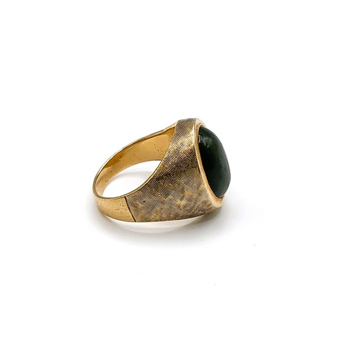 277 - A yellow metal and green hardstone gents ring, set with an oval cabochon green stone, engine-turned ... 