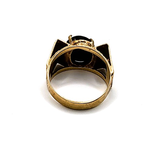 278 - A yellow metal and black onyx ring, with raised pyramid detail to shoulders, centred with an oval on... 