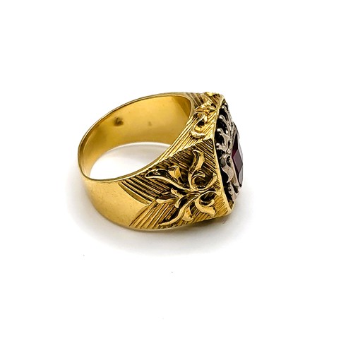 283 - An unusual yellow gold gents ring, set with a shield-cut faceted red paste gemstone, within a shield... 