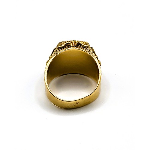 283 - An unusual yellow gold gents ring, set with a shield-cut faceted red paste gemstone, within a shield... 