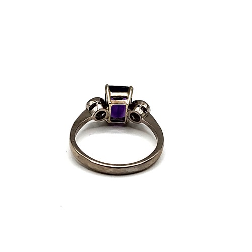 330 - An 18ct white gold, diamond, and amethyst three stone ring, set with a rectangular-cut amethyst flan... 