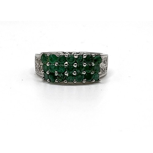 347 - An 18ct white gold, diamond, and emerald ring, set with twenty-one round-cut emeralds, the shoulders... 