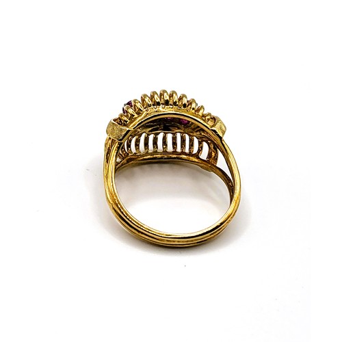 385 - A yellow metal and ruby cocktail ring, set with four round-cut rubies, in openwork ribbed mount, siz... 