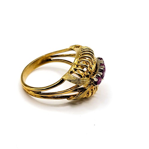 385 - A yellow metal and ruby cocktail ring, set with four round-cut rubies, in openwork ribbed mount, siz... 