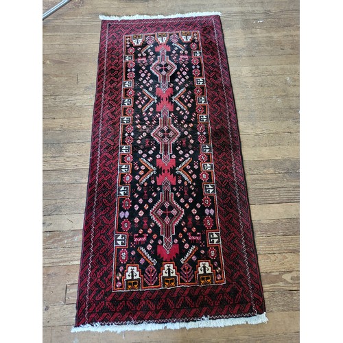 70 - A red and black ground rug with symmetric pattern detail, fringed. 208cm x 91cm