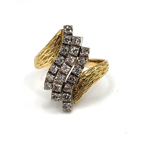 242 - A yellow metal and diamond crossover ring, the textured shoulders set with three rows of round brill... 