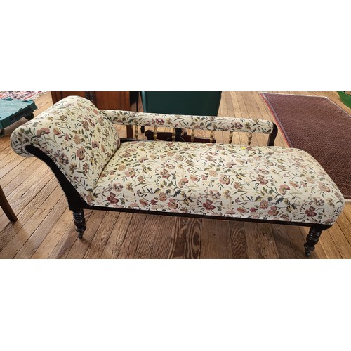 42 - A rail-back chaise longue with floral upholstery, on turned legs and casters. 66cm x 160cm x 66cm