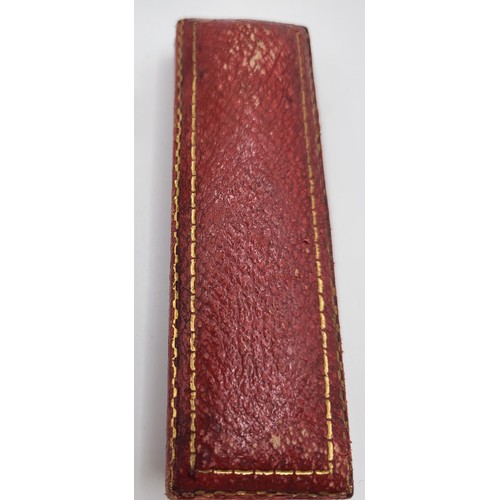 288 - A red leather tooled box with a gold unmarked stick pin with safety chain topped with a motif. 3.3gm... 