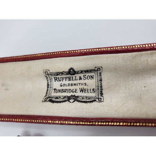 288 - A red leather tooled box with a gold unmarked stick pin with safety chain topped with a motif. 3.3gm... 