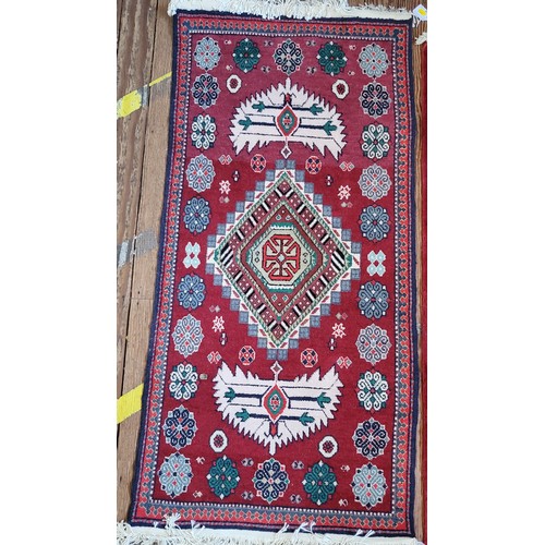 89 - A red rug with white and green diamond pattern. 130cm x 62cm.