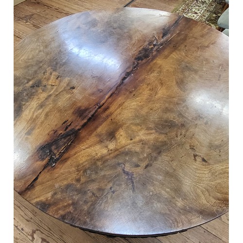 69 - A circular dining tilt table with a burr elm top (some damage) on a carved pedestal and tripod legs.... 