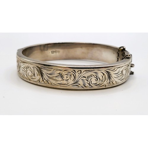 357 - A silver hinged bracelet with safety chain and foliate design on upper half. 20.8gms