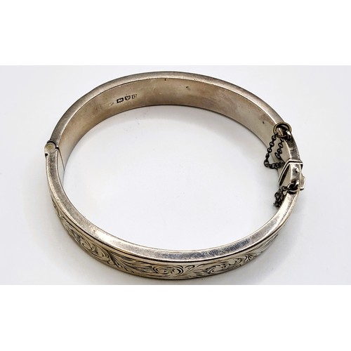 357 - A silver hinged bracelet with safety chain and foliate design on upper half. 20.8gms