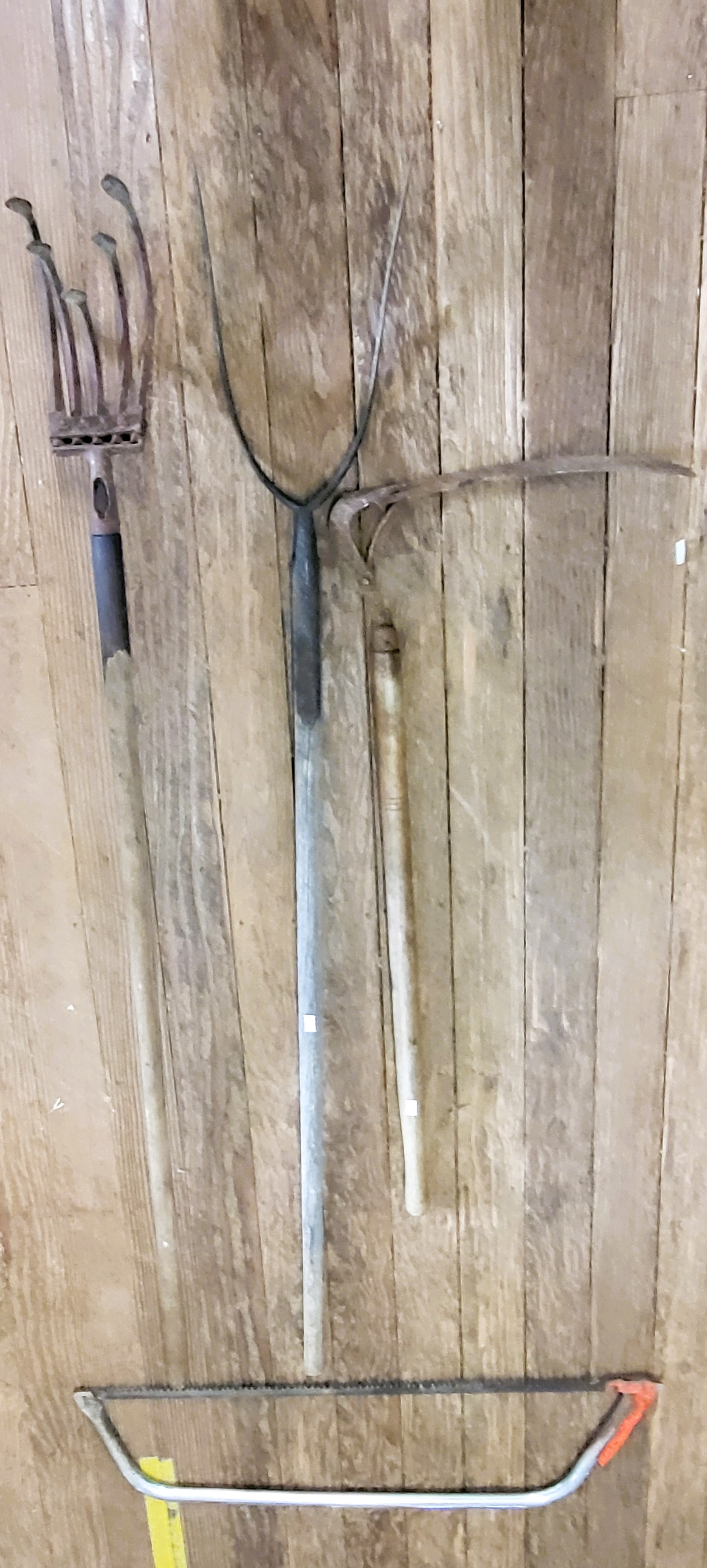 Three antique garden tools including a pitchfork, a scythe, and a ...