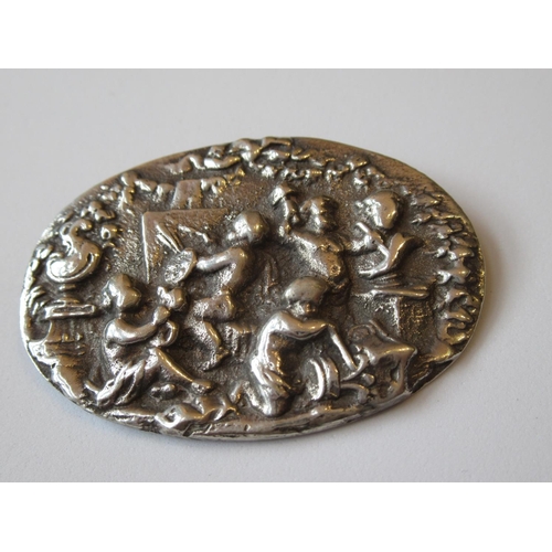 1066 - Oval white metal brooch decorated in relief with cherub artists, 2ins wide