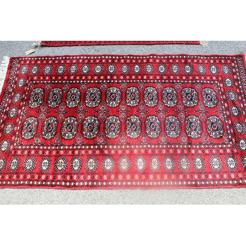4 - Two small Bokhara pattern rugs on wine ground, together with a machine Persian pattern rug