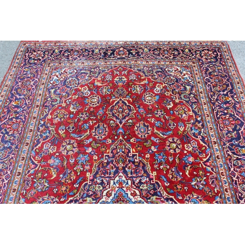 55 - Modern Kashan carpet with a medallion and all-over floral design on a red ground with borders, 9ft 8... 