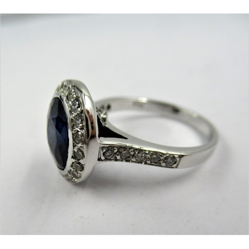 973 - 18ct White gold ring, the central oval sapphire surrounded by diamonds, the shoulders inset with dia... 