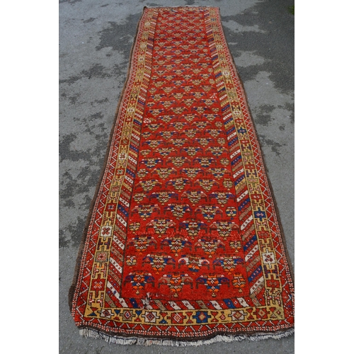 11 - Kazak runner with an all-over stylised flowerhead design on a red ground with borders, 12ft 10ins x ... 
