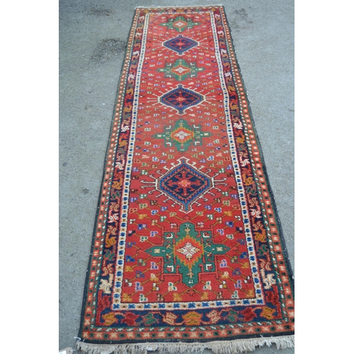 29 - Karaja runner with seven hooked medallions on a brick red ground with borders, 9ft 10ins x 2ft 10ins... 