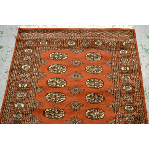 32 - Pakistan rug of Turkoman design with two rows of gols on a rust ground with borders, 150cms x 90cms