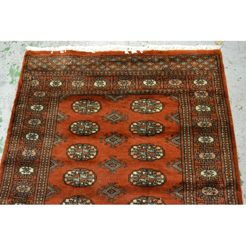 32 - Pakistan rug of Turkoman design with two rows of gols on a rust ground with borders, 150cms x 90cms