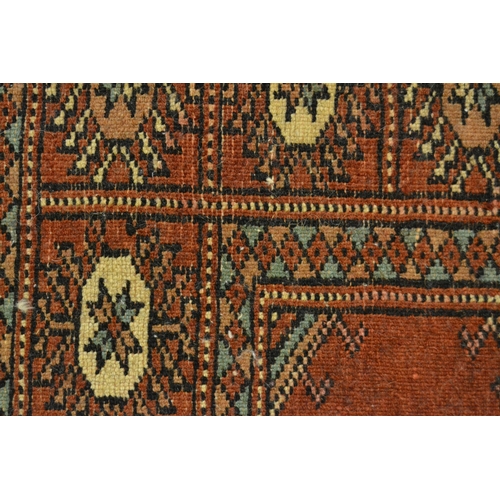 32 - Pakistan rug of Turkoman design with two rows of gols on a rust ground with borders, 150cms x 90cms