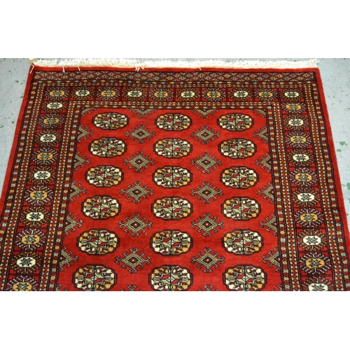 44 - Pakistan rug of Turkoman design with three rows of gols on red ground with borders, 182cms x 124cms