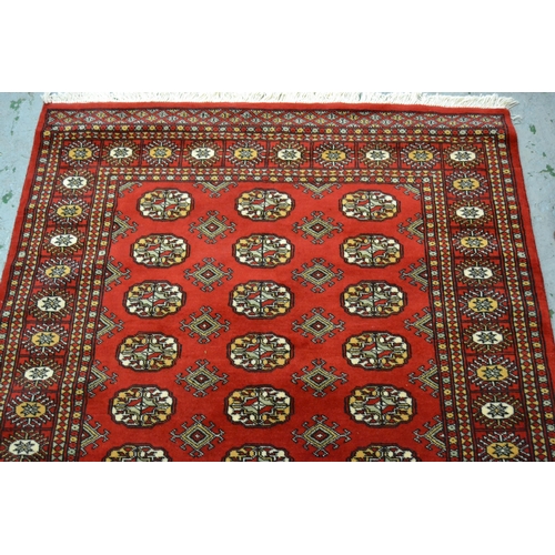 44 - Pakistan rug of Turkoman design with three rows of gols on red ground with borders, 182cms x 124cms