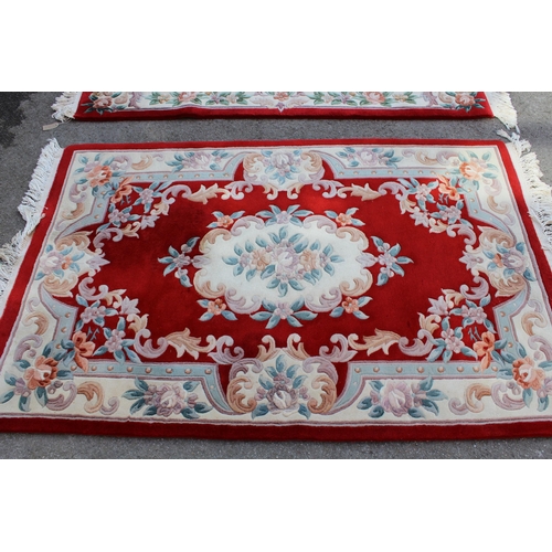 23 - Pair of Chinese rugs with medallion and floral design on a red ground, 185cms x 125cms