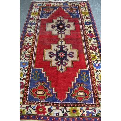 11 - Anatolian rug with a twin medallion design on a red ground with borders, 221cms x 122cms