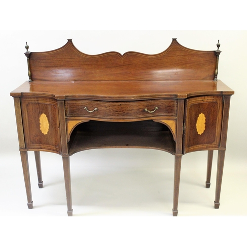 Edwardian mahogany line and shell inlaid serpentine shaped sideboard, the shaped back with brass baluster uprights above a central drawer and alcove, flanked by two cupboard doors raised on square tapering supports with spade feet, 153cms wide