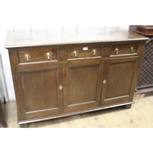 1439 - Oak dresser base, the moulded top above three short drawers with brass drop handles, with two panell... 