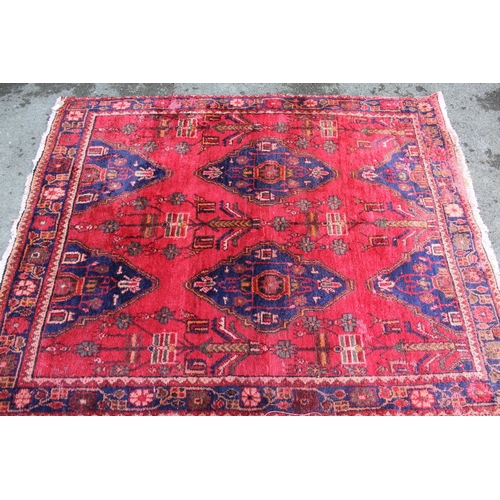 8 - Hamadan rug with a repeating medallion design and stylised floral designs on a red ground with borde... 