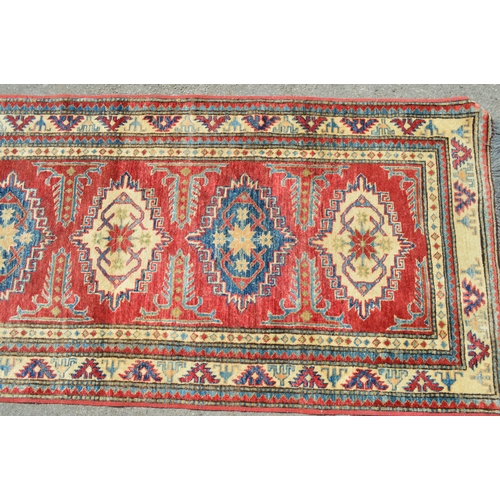 18 - Indo Persian runner with a repeating hooked medallion design on a red ground with borders, 288 x 83c... 