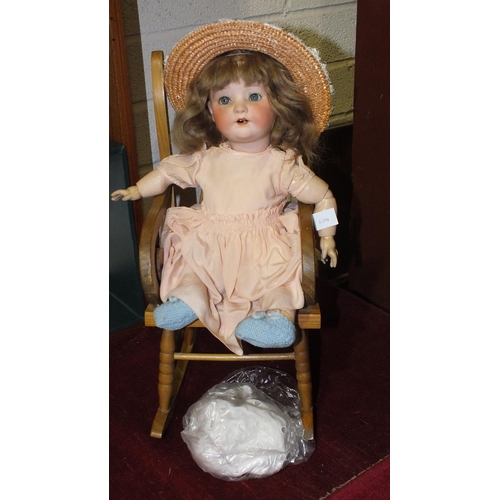 159 - A Continental bisque-headed doll with sleeping eyes, (head cracked), in wood rocking chair.