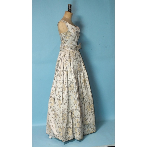 530 - A 1950's ivory floral brocade evening dress, sleeveless, with full pleated skirt and bow waist band,... 