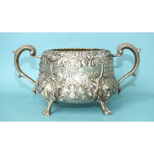 520 - A two-handled sugar basin profusely-decorated and chased with foliage, raised on cast mask feet, wit... 