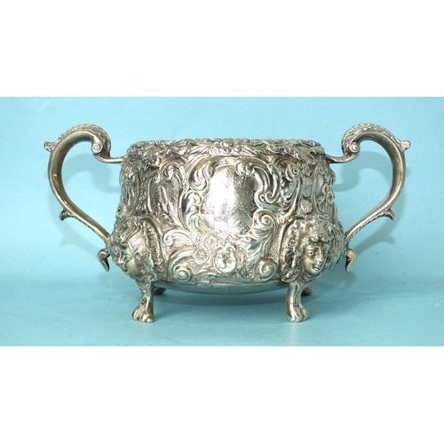 520 - A two-handled sugar basin profusely-decorated and chased with foliage, raised on cast mask feet, wit... 