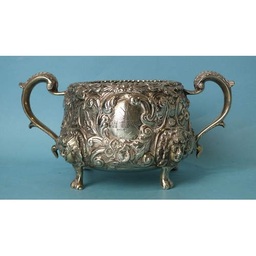 520 - A two-handled sugar basin profusely-decorated and chased with foliage, raised on cast mask feet, wit... 