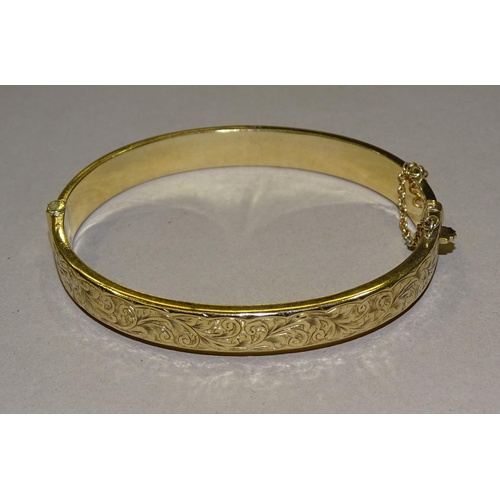 211 - A 9ct gold hinged bangle with engraved scroll decoration, 8mm wide, 9.5g.