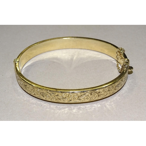 136 - A 9ct gold hinged bangle with engraved scroll decoration, 8mm wide, 9.5g.