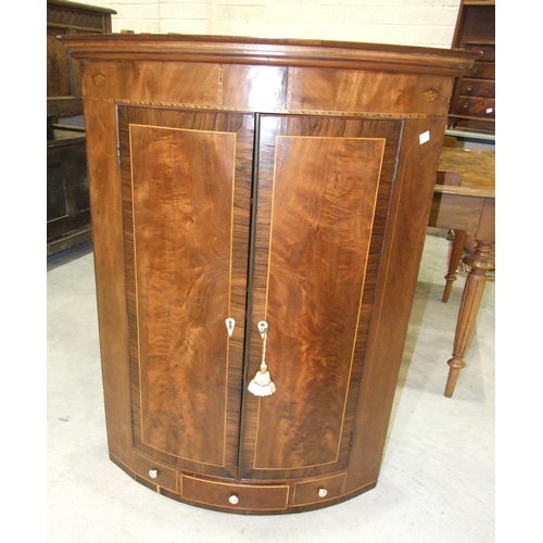 12 - A Georgian mahogany bow-fronted corner cupboard, having a pair of rosewood-banded doors above a smal... 