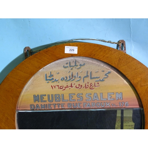 229 - An Egyptian walnut advertising mirror and coat rack of circular form, the mirror painted with Arabic... 